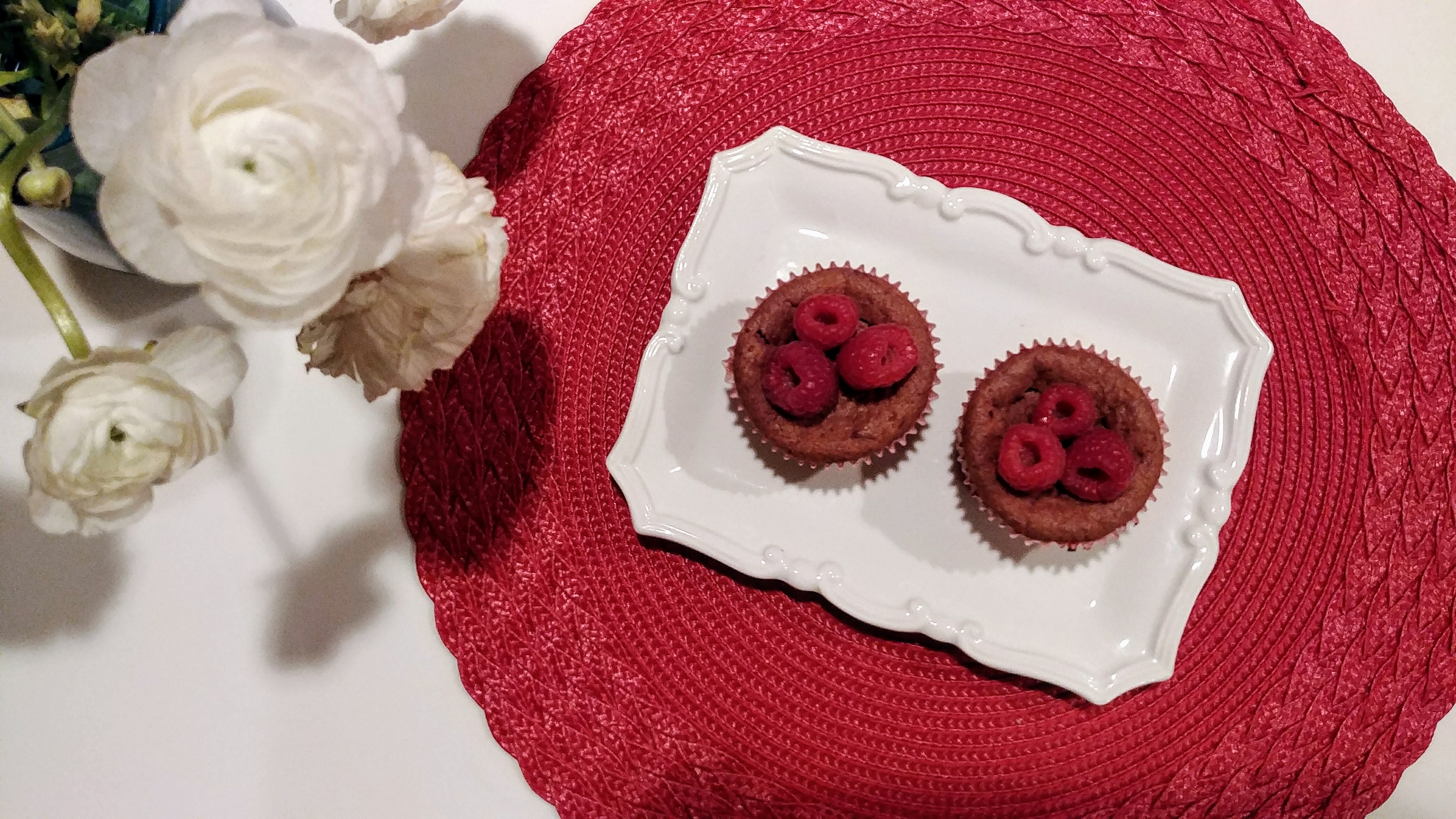 Raspberry Cupcakes topped with fresh raspberries next to white flowers on table